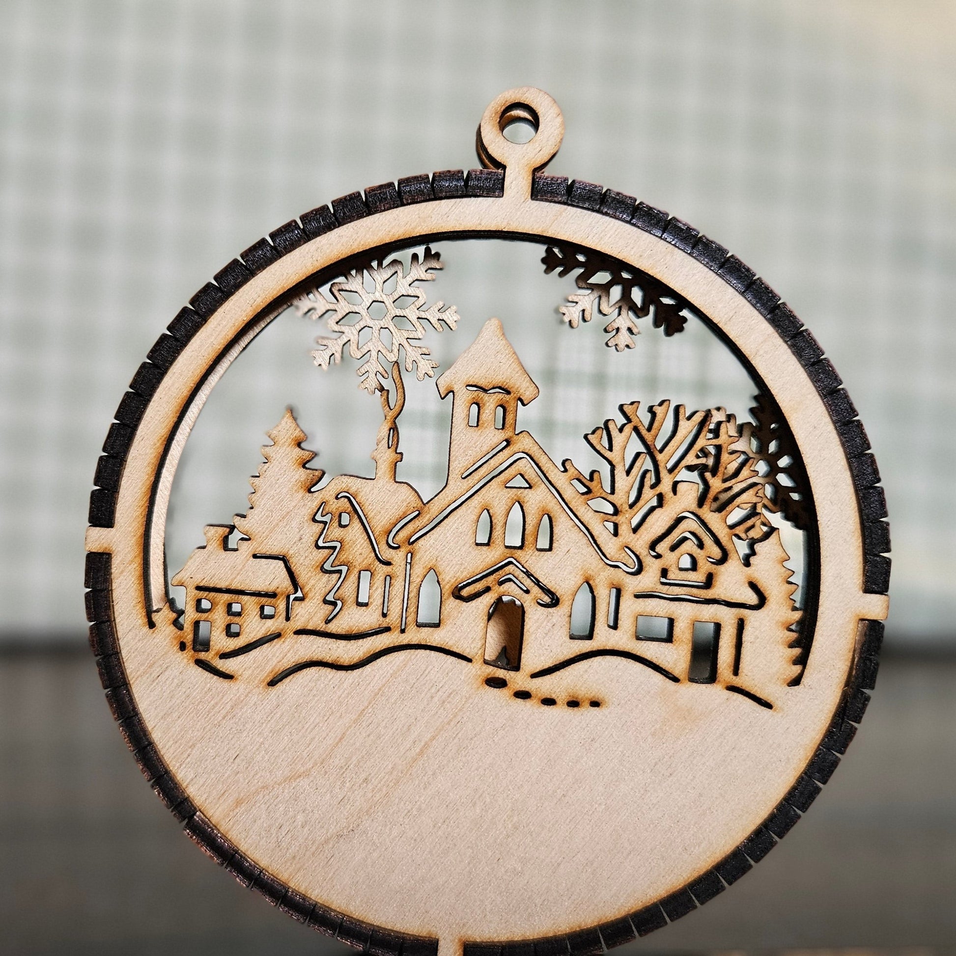 A two-layer wooden ornament featuring a truck carrying a Christmas Tree in the foreground and a winter village scene in the background.